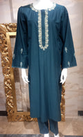 Teal dress with white embroidery on a mannequin in front of a decorative mirror.