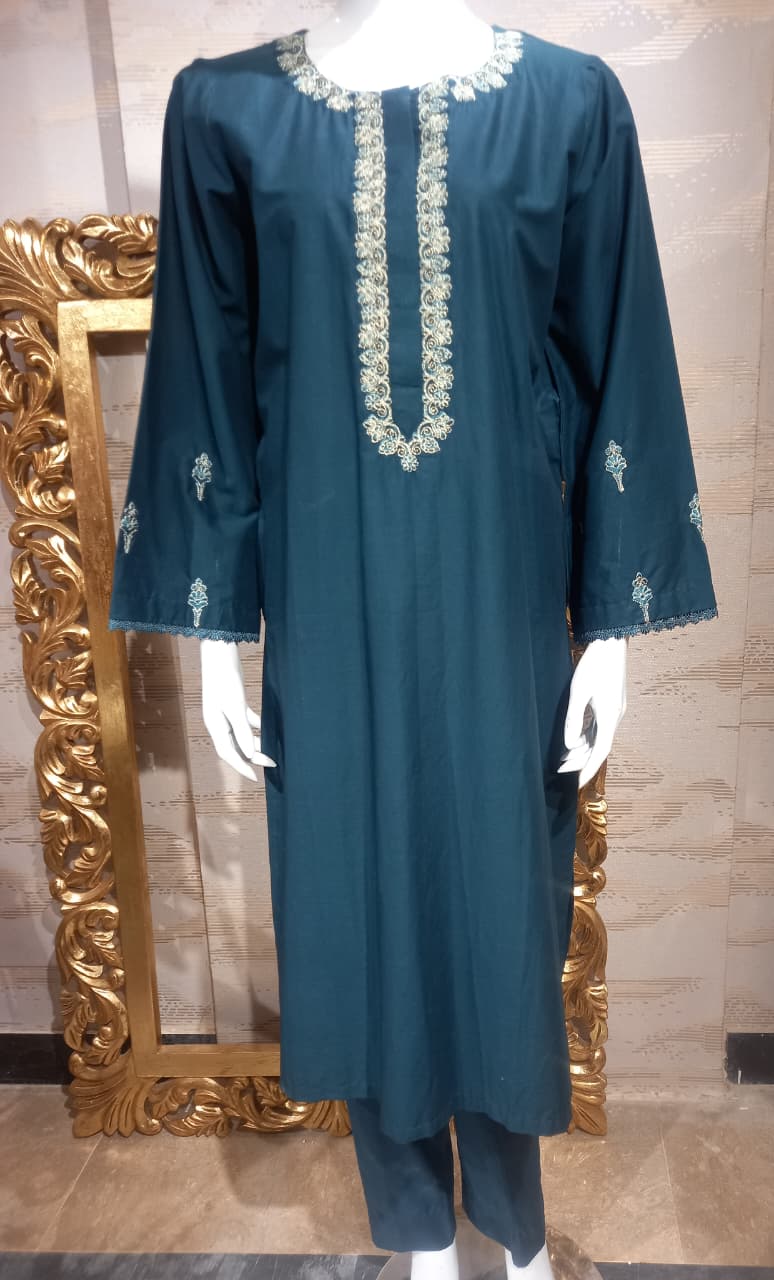 Teal dress with white embroidery on a mannequin in front of a decorative mirror.